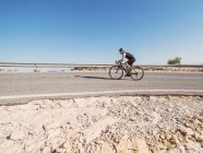 Homem saudável andar de bicicleta na estrada em dia ensolarado com paisagem estéril no fundo — Fotografia de Stock