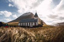 Маленькая церковь, стоящая в сухой долине около высокого холма на Фарерском острове — стоковое фото