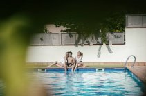 Grupos de amigos tomando el sol junto a la piscina mientras beben cerveza en un día de verano. - foto de stock