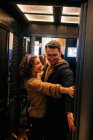 Вид сбоку веселый молодой человек и женщина, держащие дверь лифта и улыбающиеся во время романтического свидания — стоковое фото