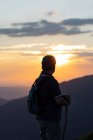 Silhouette di vista posteriore di un uomo anziano con zaino e bastone di legno trekking contemplando incredibile paesaggio montano — Foto stock