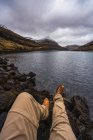 Неузнаваемый человек, сидящий у озера, показывая ноги, расслабляющие на Фарерском острове — стоковое фото