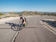 Здоровий чоловік їде на велосипеді на гірській прибережній дорозі в сонячний день — стокове фото