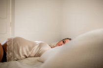 Mulher grávida em roupa interior relaxante em cama confortável em casa — Fotografia de Stock