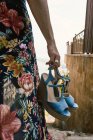 Closeup of woman in floral dress holding fashionable blue wedge heels standing on street — Stock Photo