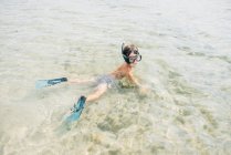 Garçon portant des palmes et masque de plongée tout en nageant et en explorant le fond en eau peu profonde — Photo de stock
