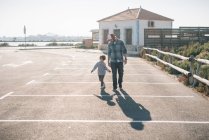 Erwachsener Mann mit spielerischem Sohn in Freizeitkleidung geht bei Sonnenschein auf Parkplatz der Straße — Stockfoto