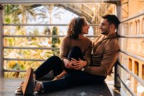 Allegro giovane uomo e donna che si abbracciano e si guardano mentre si siedono all'interno del padiglione illuminato durante la data — Foto stock