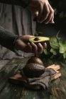 Human hands holding halved avocado over wooden table — Stock Photo