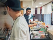 Vista laterale di multirazziale giovani uomini cucina piatto giapponese chiamato ramen in ristorante asiatico e guardando in macchina fotografica — Foto stock
