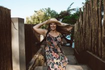 Glückliche erwachsene Frau mit Strohhut und floralem Kleid, die sich auf der sonnigen Straße dreht — Stockfoto