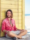 Cheerful bearded man in casual outfit sitting against yellow wall on resort — Stock Photo
