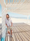 Bonito homem barbudo olhando para longe enquanto se inclina no pilar de gazebo branco na praia arenosa — Fotografia de Stock