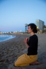 Vista lateral do homem realizando meditação de ioga na praia de areia ao pôr do sol à noite — Fotografia de Stock