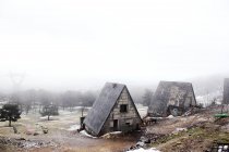 Погодные старые коттеджи в заснеженной сельской местности в туманный день — стоковое фото