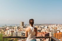 Rückansicht einer jungen Frau im weißen T-Shirt, die bei hellem Tag den Blick vom Balkon auf die Stadt in Alicante genießt — Stockfoto