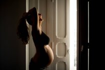 Seitenansicht einer gut gelaunten Schwangeren im BH, die vor offener Tür zu Hause steht — Stockfoto