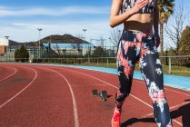 Primo piano di forte atleta donna in abbigliamento sportivo che corre veloce contro il cielo blu nella giornata di sole sullo stadio — Foto stock