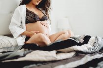 Close up of expecting baby sitting on bed at home — стоковое фото