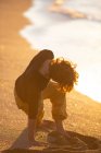Visão traseira do homem esportivo em calças amarelas descalço realizando exercícios de meditação de ioga na praia de areia ao pôr do sol à noite — Fotografia de Stock