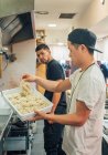 Seitenansicht von jungen multirassischen Männern, die Nudeln vom Tablett nehmen, um Ramen im Restaurant zu kochen — Stockfoto