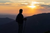 Silhouette of back view of a senior man with back pack and wooden stick hiking contemplating amazing mountain landscape — Stock Photo