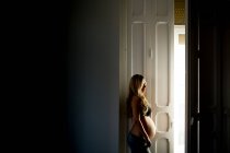 Nachdenkliche Schwangere im BH steht vor offener Tür zu Hause — Stockfoto