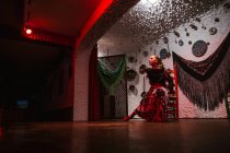 Tänzerin im Flamenco-Kostüm sitzt in Tanzhaltung im ethnischen Raum mit antiken Gegenständen an der Wand — Stockfoto