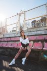 Slim jovem mulher em sportswear olhando para longe enquanto sentado no assento do estádio grungy durante o treinamento — Fotografia de Stock