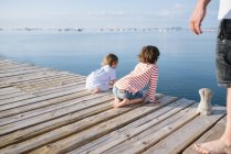 Crop man and adorable curious boy with toddler sister sitting on pier observing nature — Stock Photo