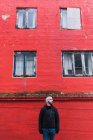 Hombre barbudo mirando hacia otro lado mientras estaba parado frente al edificio rojo en la isla Faroe - foto de stock