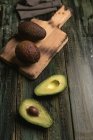 Свежие целые и наполовину авокадо на деревянном столе — стоковое фото