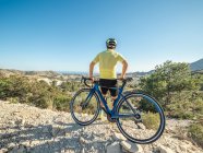 Healthy man resting and enjoying view with bicycle on mountain road in a sunny day — Stock Photo
