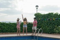 Група друзів, які проводять вечірку біля басейну, танцюють, сміються і п'ють коктейлі — стокове фото