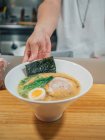 Hand of man putting bowl of fresh cooked traditional Japanese dish on wooden counter in restaurant — Stock Photo