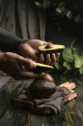 Mani umane che tengono avocado dimezzato su tavolo di legno — Foto stock