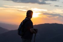 Silhouette der Rückenansicht eines älteren Mannes mit Rucksack und Holzstab beim Wandern mit Blick auf die atemberaubende Berglandschaft — Stockfoto
