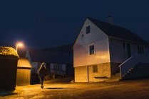 Женщина смотрит в сторону ночью на улице небольшой деревни со светом на Фарерском острове — стоковое фото