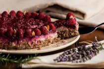 Нарезанный сочный фруктовый торт с малиной на белой тарелке на деревянном столе украшенном лавандовым букетом — стоковое фото
