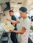 Vista lateral de jovens homens multirraciais tomando macarrão de bandeja para cozinhar ramen no restaurante — Fotografia de Stock