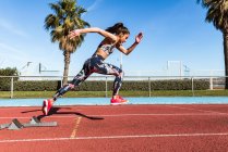 Сильна жінка-спортсменка в спортивному одязі працює швидко проти блакитного неба в сонячний день на стадіоні — стокове фото
