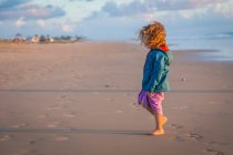 Lockiges Kind in gestreiften Spaziergängen am Strand auf verschwommenem Naturhintergrund — Stockfoto