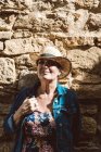 Женщина в соломенной шляпе прислонилась к каменной стене на улице средневековой деревни — стоковое фото