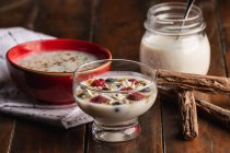 Сверху аппетитный ароматный йогурт с малиновым овсянкой из стекла и красными чашами, украшенными коричными палочками на деревянном фоне — стоковое фото