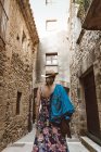 Rückansicht einer unkenntlichen Frau mit Kleid und Hut, die auf der Straße einer mittelalterlichen Stadt spaziert — Stockfoto