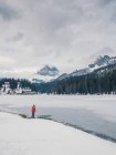 Persona irreconocible parada en la nieve rodeada de bosques y montañas - foto de stock