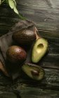 Fresh whole and halved avocados on wooden table — Stock Photo