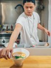 Giovane uomo mettendo ciotole di fresco cucinato piatto tradizionale giapponese sul bancone di legno nel ristorante — Foto stock