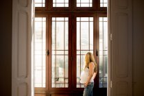 Вдумлива вагітна жінка в повсякденний одяг стоячи біля вікна будинку — стокове фото