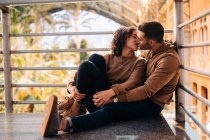 Jovem alegre e mulher abraçando e beijando-se olhando um para o outro enquanto sentado dentro do pavilhão iluminado durante a data — Fotografia de Stock